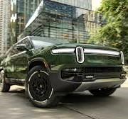 शहर की सड़क पर चलती हुई गहरे हरे रंग की शानदार रिवियन R1 इलेक्ट्रिक एसयूवी